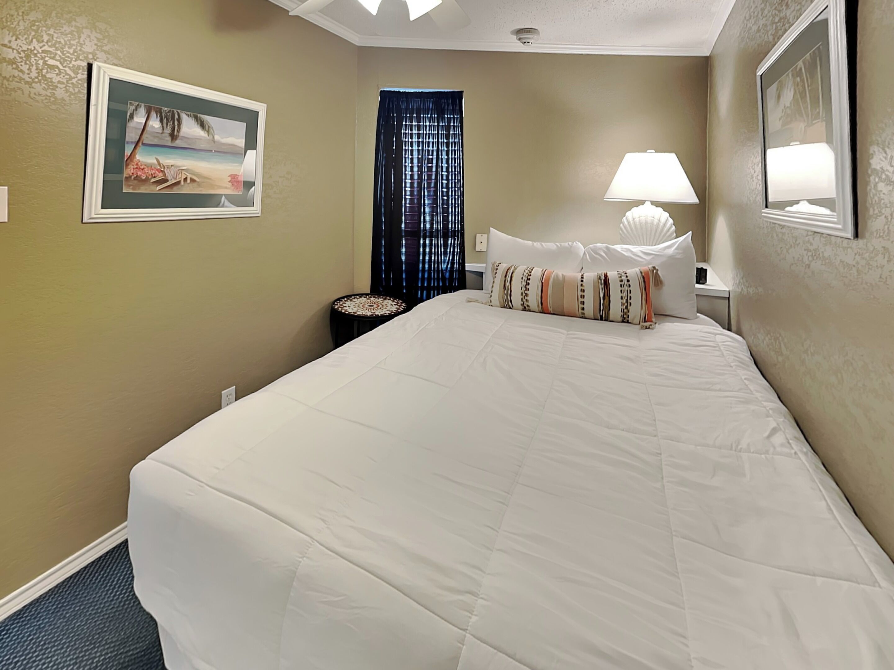 A hotel room with a large bed, a nightstand with a lamp, a small table, and a painting on the wall.
