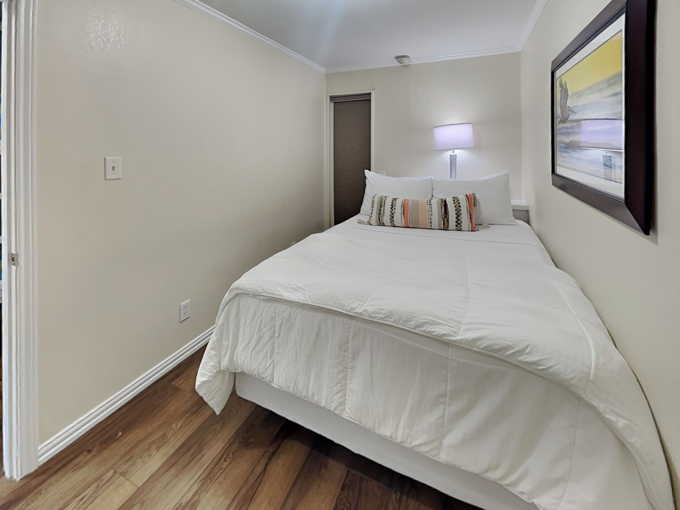 Un dormitorio con cama, mesita de noche, lámpara y un cuadro en la pared.