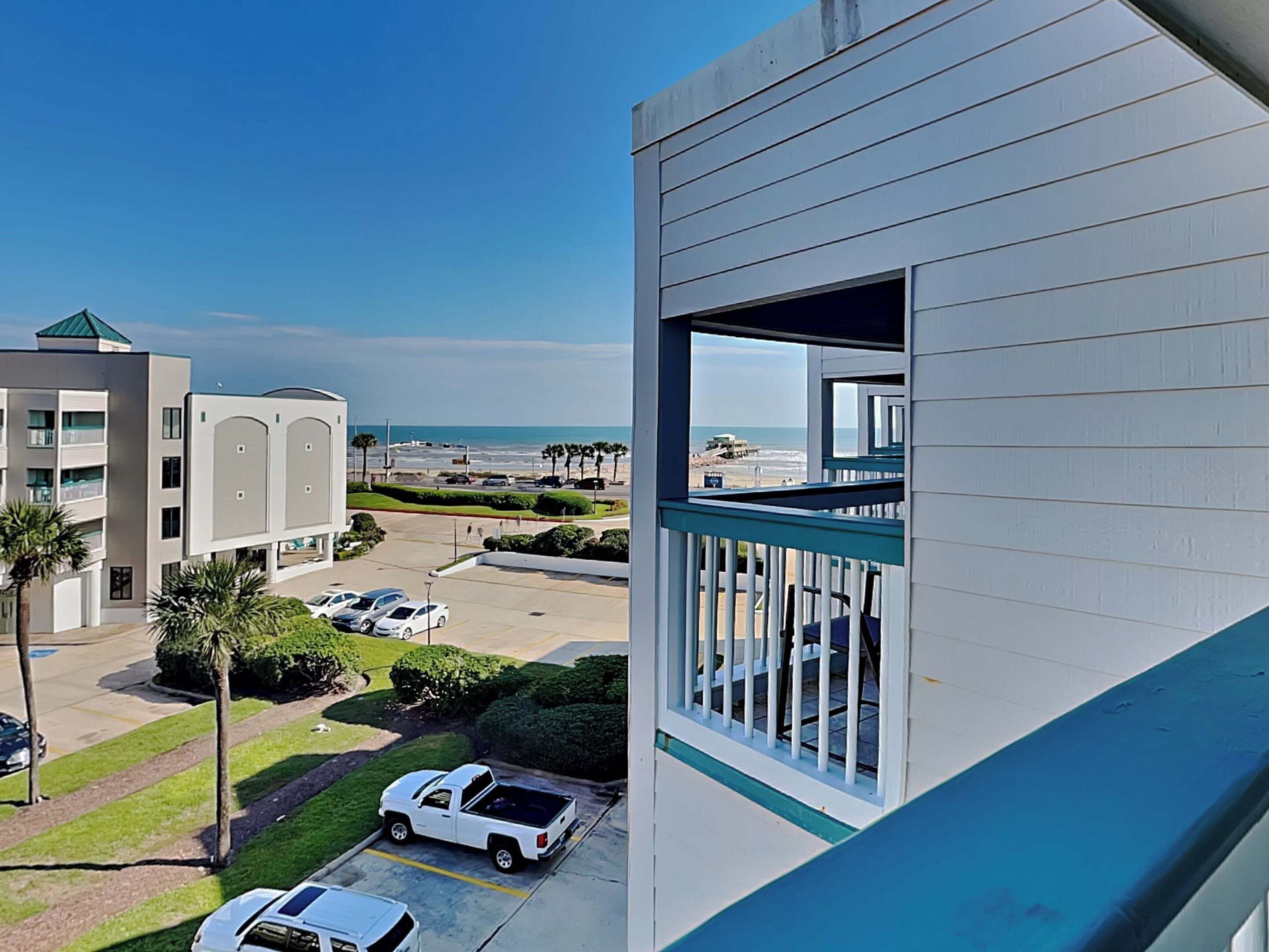 A modern building with a balcony overlooking a parking area and a beach.