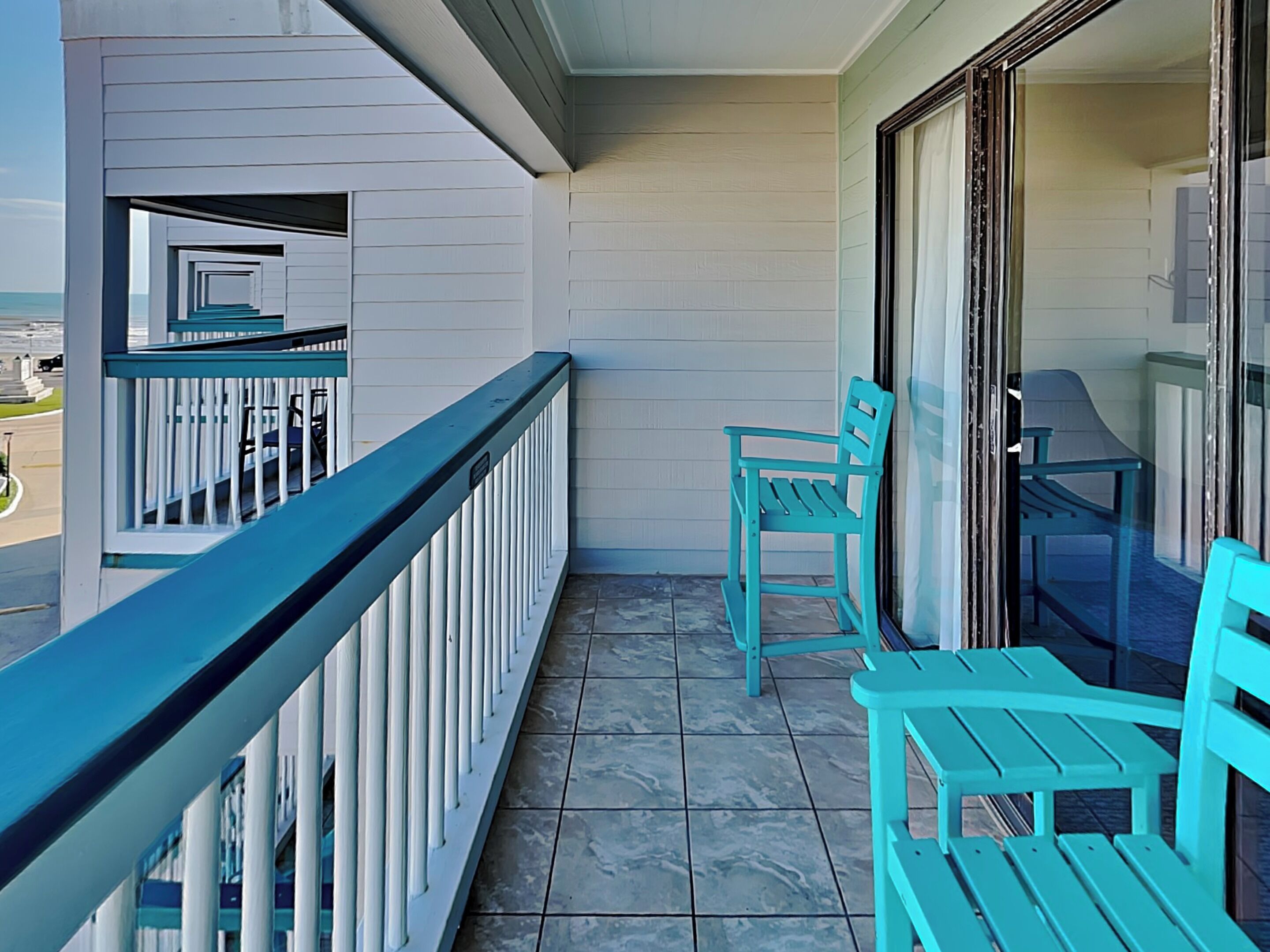 Un balcon doté d’un sol carrelé, d’une balustrade et de deux chaises turquoise.