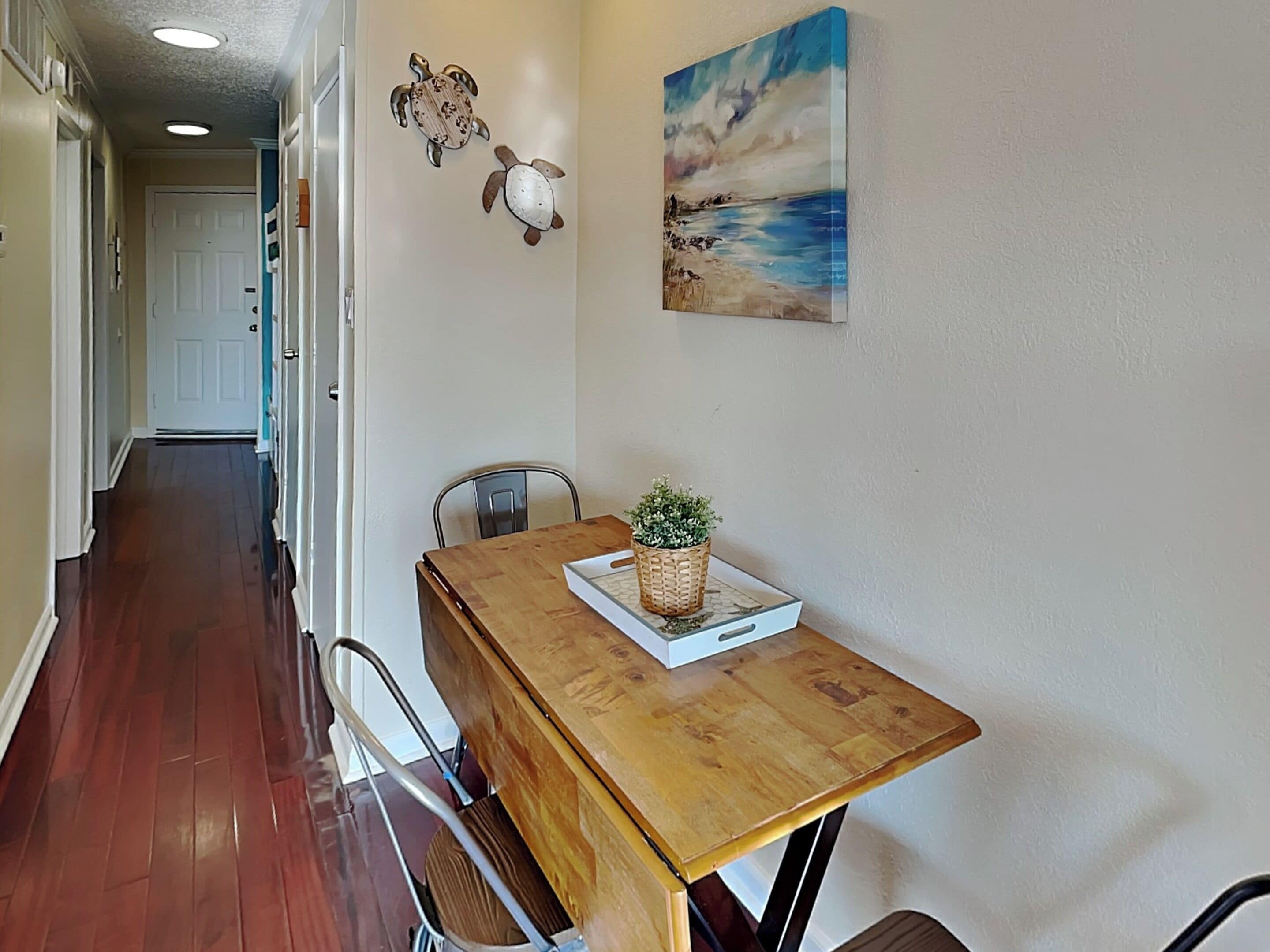 A hallway with a wooden dining table, chairs, a potted plant, and artwork on the walls.