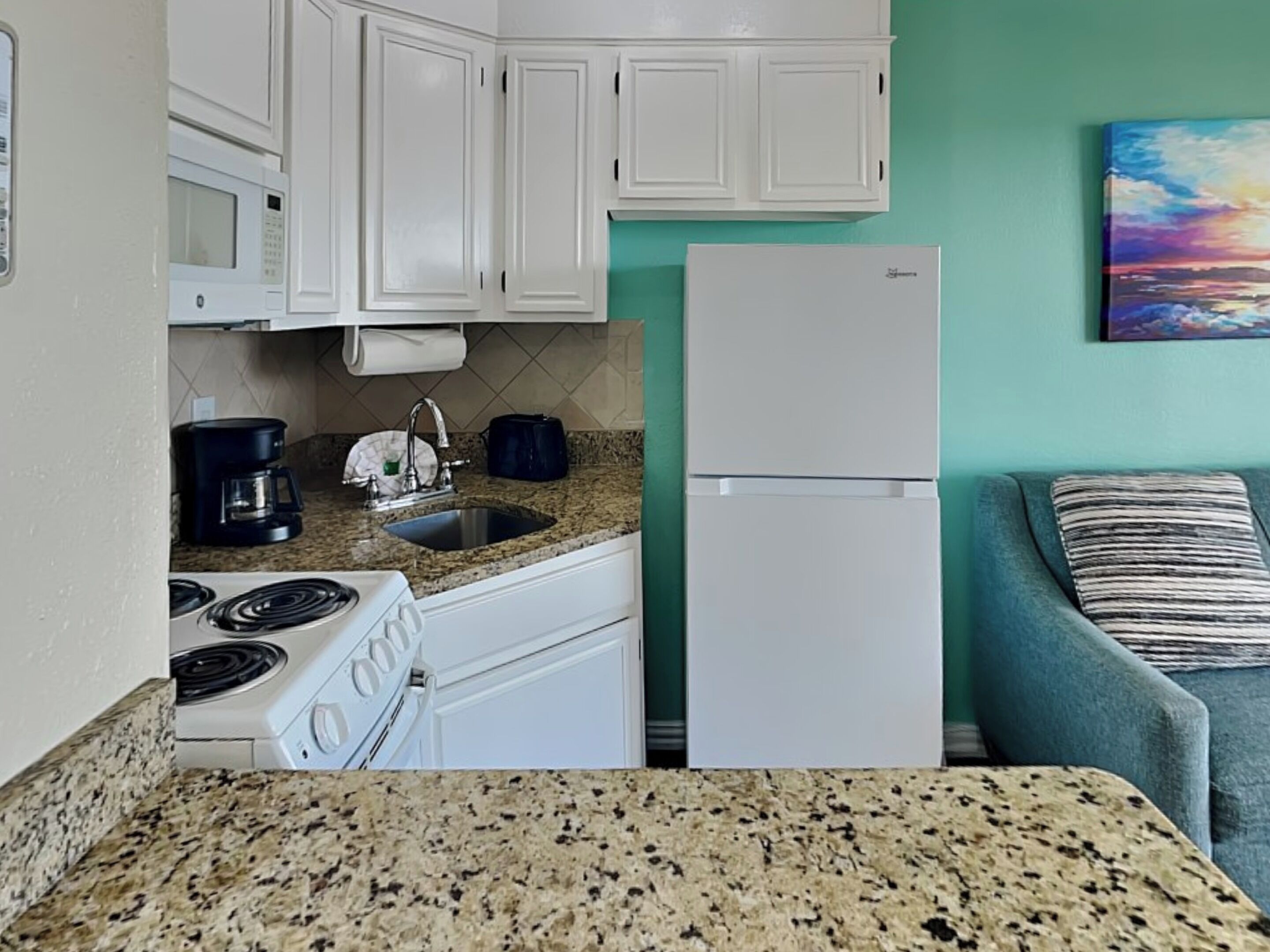 A kitchen with white cabinets, a granite countertop, a stove, a sink, and a refrigerator.