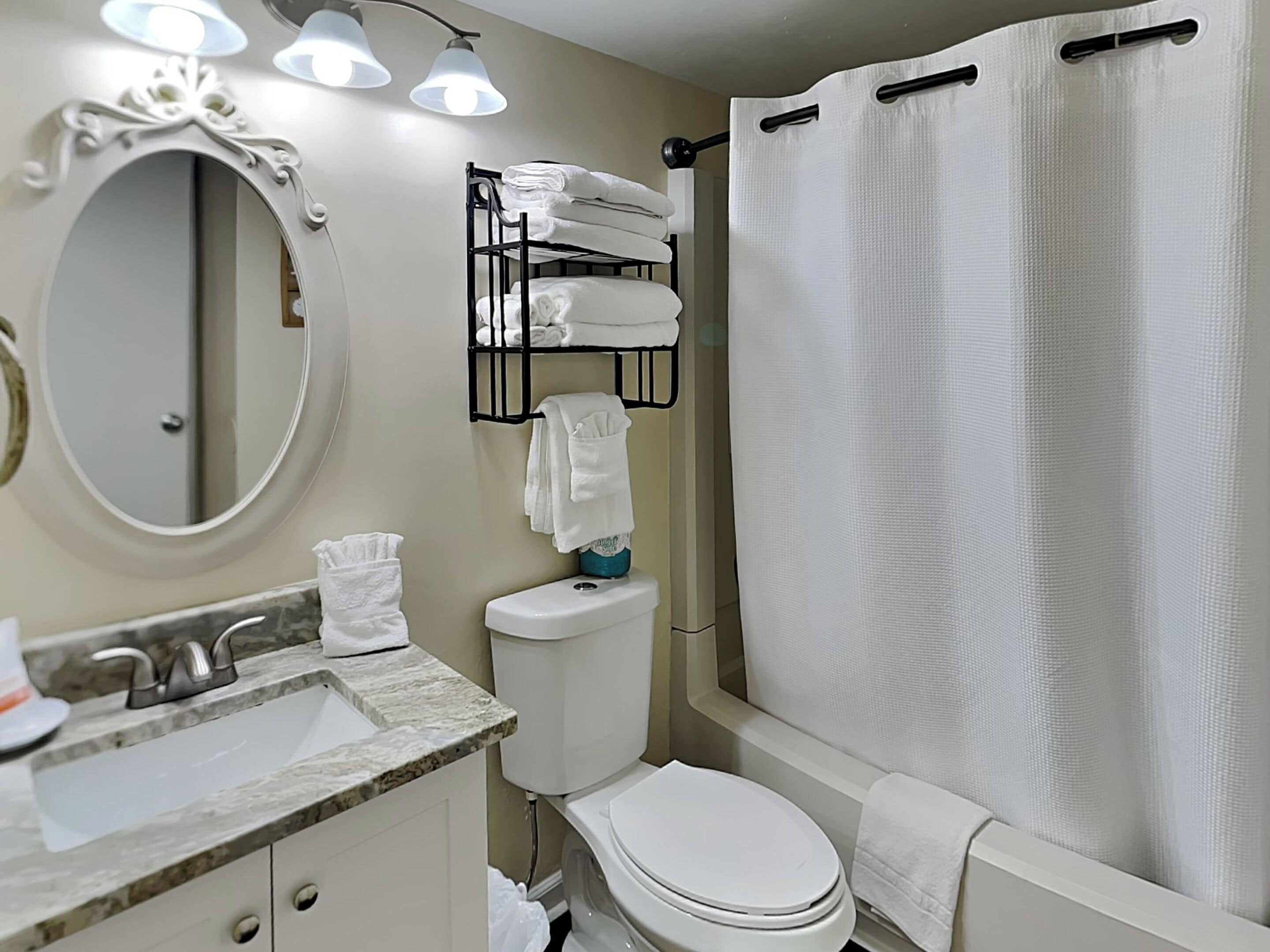 A bathroom with a sink, toilet, and a shower curtain. There is a towel rack with towels and a mirror above the sink.