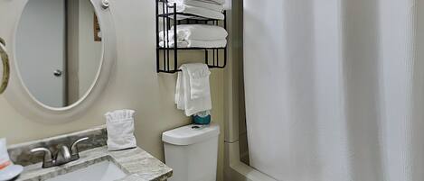 A bathroom with a sink, toilet, and a shower curtain. There is a towel rack with towels and a mirror above the sink.