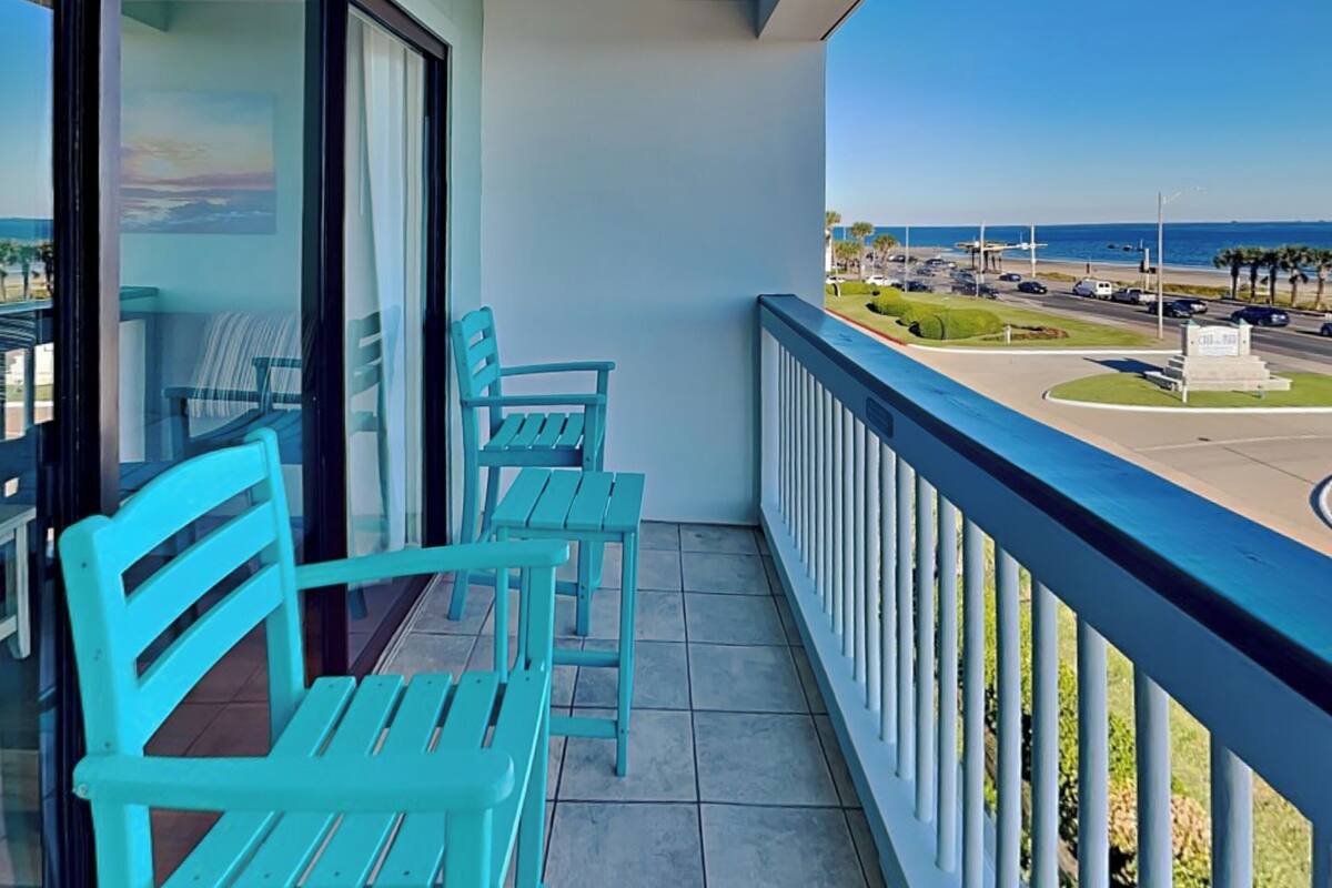 A balcony with turquoise chairs and a view of a road and ocean.