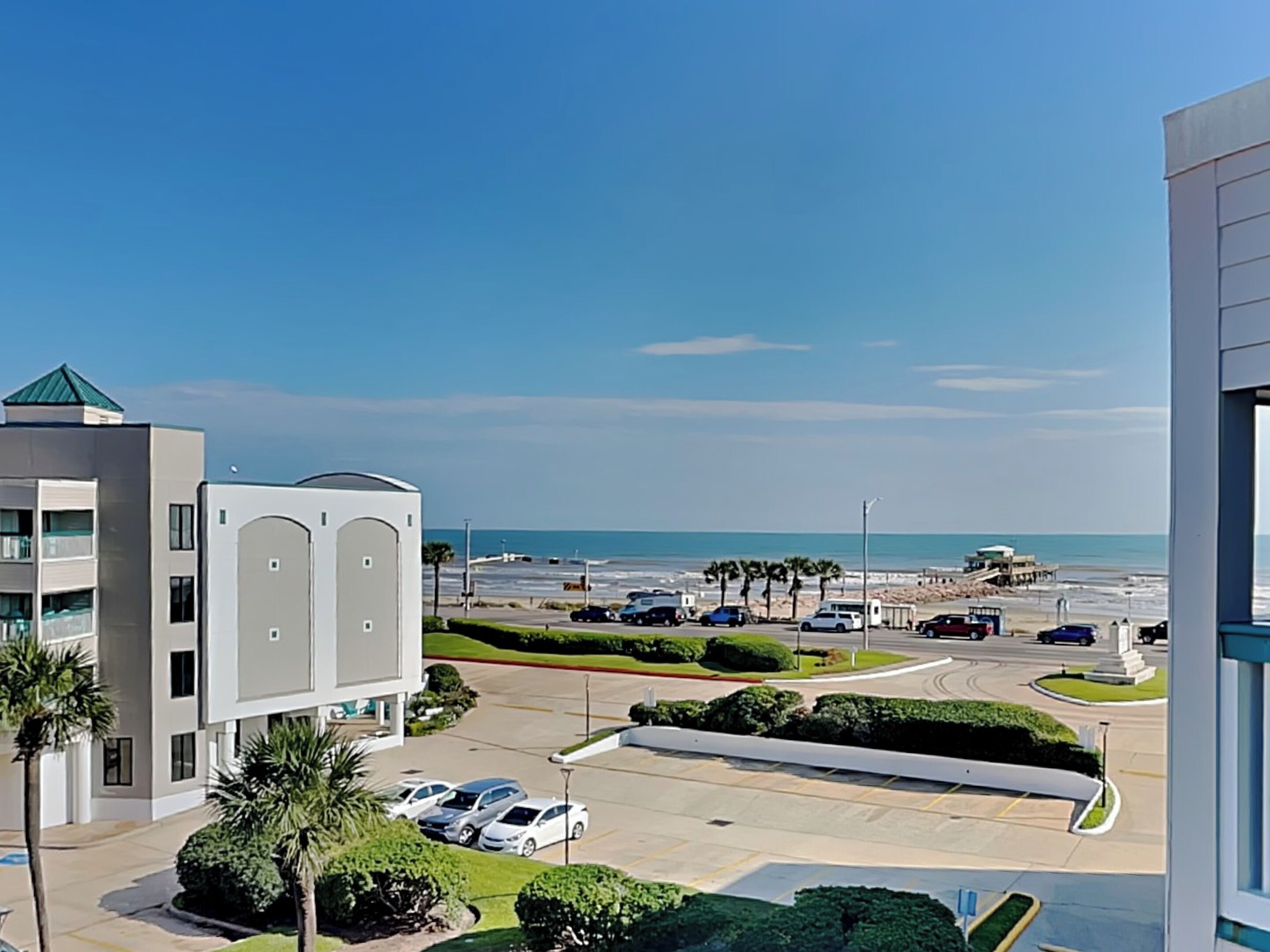 A coastal hotel with a parking lot, a view of the beach, and a clear sky.