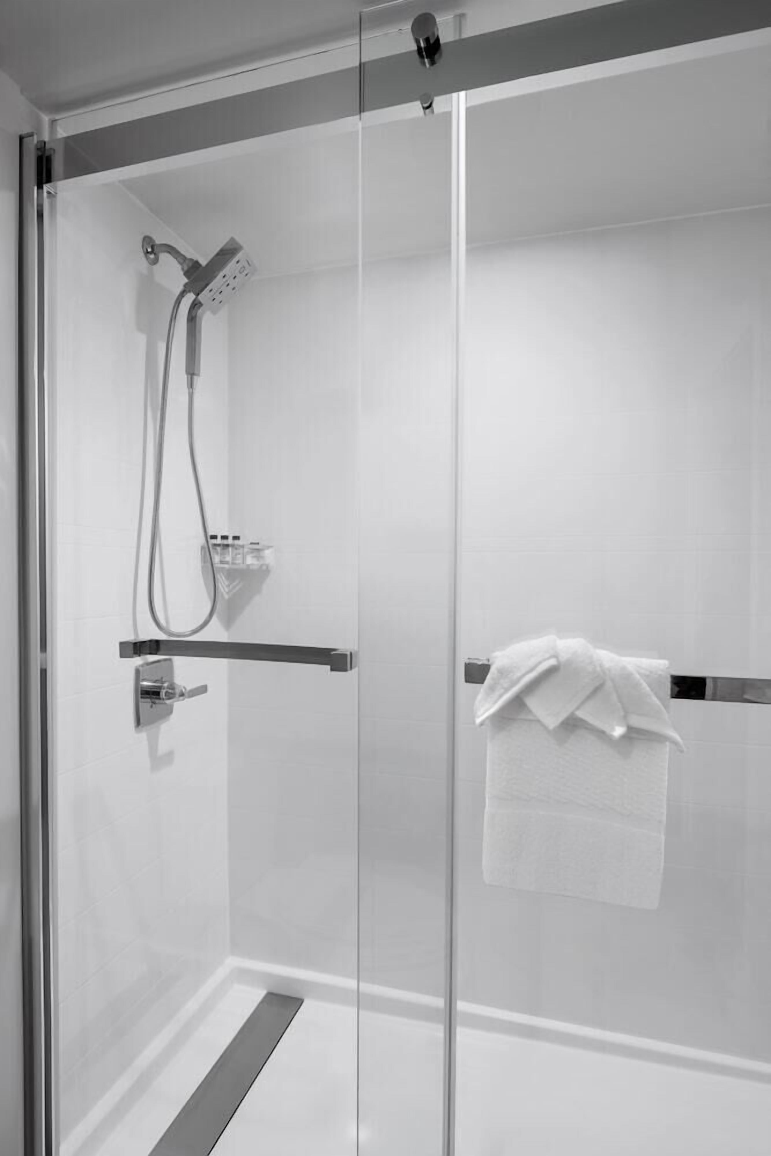 Cabina doccia in vetro con soffione a mano, portasci con asciugamano e pannello comandi.