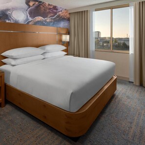 A hotel room with a large bed, a headboard, a nightstand, a window with curtains, and a cityscape view. - Delta Hotels Santa Clara Silicon Valley (Santa Clara)