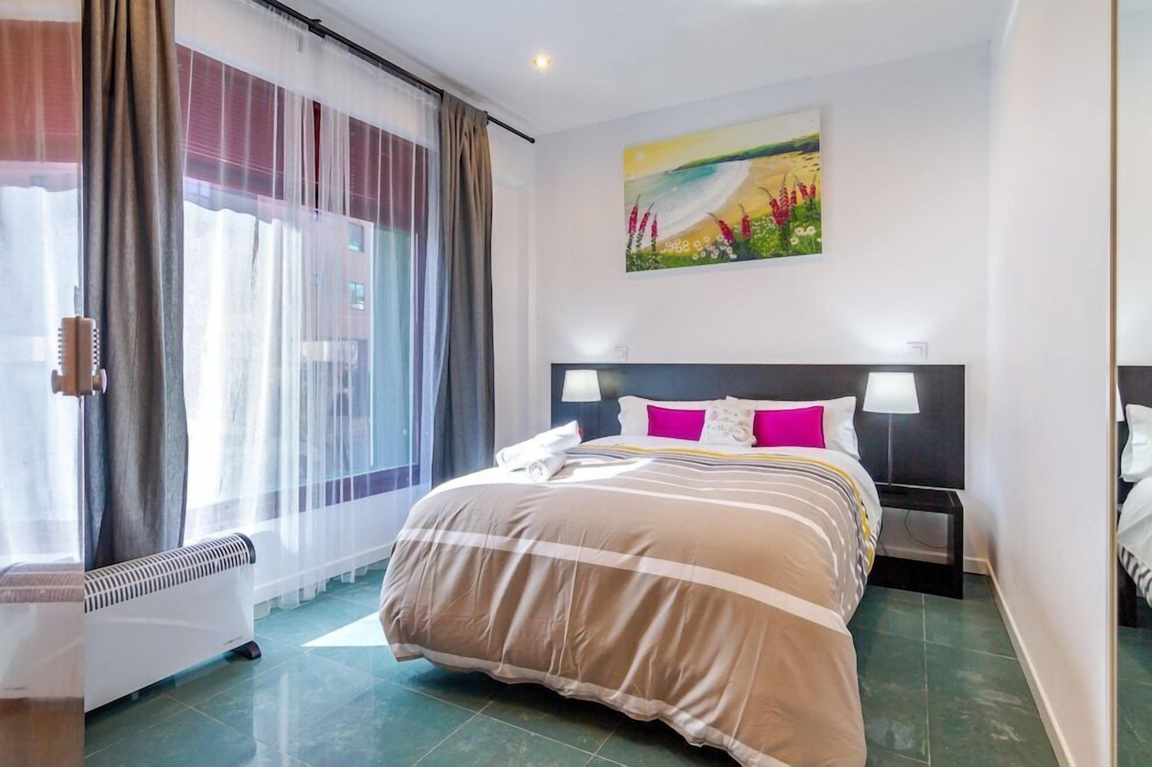 Quarto de hotel com uma cama grande, um quadro na parede e uma janela com cortinas.