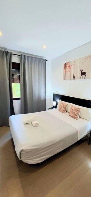 A neatly made bed with a white duvet and two pillows, a headboard, and a window with grey curtains. - A&Z Javier Cabrini (Madrid)