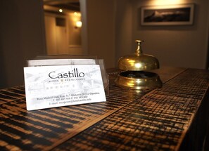 En hotellreception med en skylt med texten ”Castillo Hotel Restaurante” och en mässingsklocka.