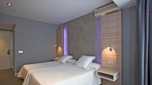 A hotel room with two beds, a built-in shelf, an air conditioning unit, and a door. - Castillo Hotel (Olaberria)