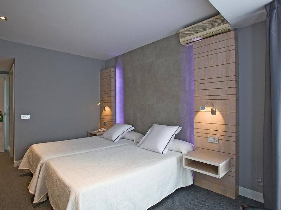 Habitación de hotel con dos camas, estante empotrado, unidad de aire acondicionado y una puerta.