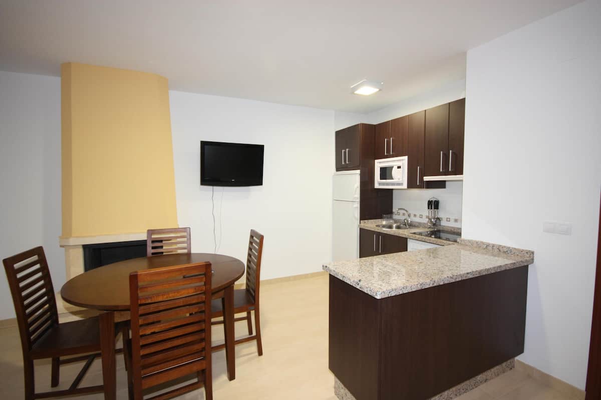 A compact kitchen with a dining area, a flat-screen TV mounted on the wall, and a built-in microwave.