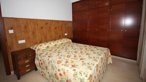A bedroom with a wooden headboard, a bed with floral bedding, a wooden nightstand, and a large wardrobe. - Campillo Apartamentos Rurales (La Iruela)