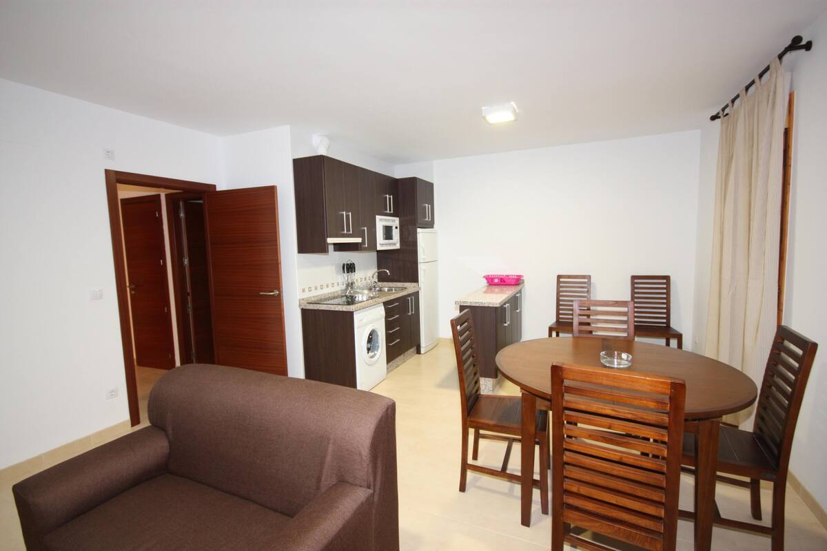 A compact living space with a kitchenette, a dining area with wooden furniture, and a brown sofa.