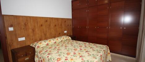 A bedroom with a wooden headboard, a bed with floral bedding, a wooden nightstand, and a large wardrobe.