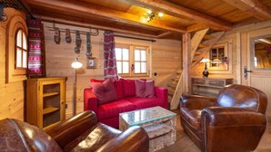 Interior acogedor de una cabaña de troncos con un sofá de cuadros rojos, sillones de cuero, una mesa de centro de vidrio y un armario de madera.