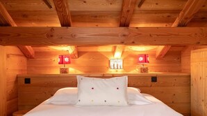 Una habitación cálida de cabaña de madera con una cama, dos lámparas rojas y una pequeña mesa con una vela.