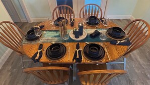 Une table de salle à manger ronde en bois, avec des assiettes noires, des couverts en argent et un set de table vert.