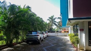 A paved pathway with parked cars, palm trees, and a building with an 'EXIT' sign. - Relax Holiday Home (Madgaon)
