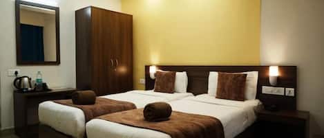 A hotel room with two beds, a wardrobe, a desk with a kettle, and a mirror.