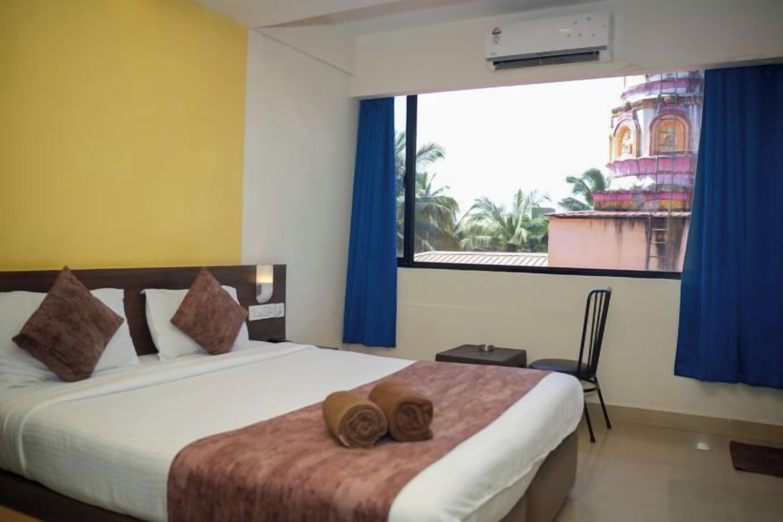 Une chambre d’hôtel avec un lit, une chaise, une fenêtre avec des rideaux et un appareil de climatisation.