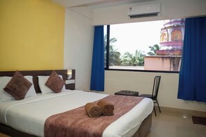 A hotel room with a bed, a chair, a window with curtains, and an air conditioning unit. - Relax Holiday Home (Madgaon)