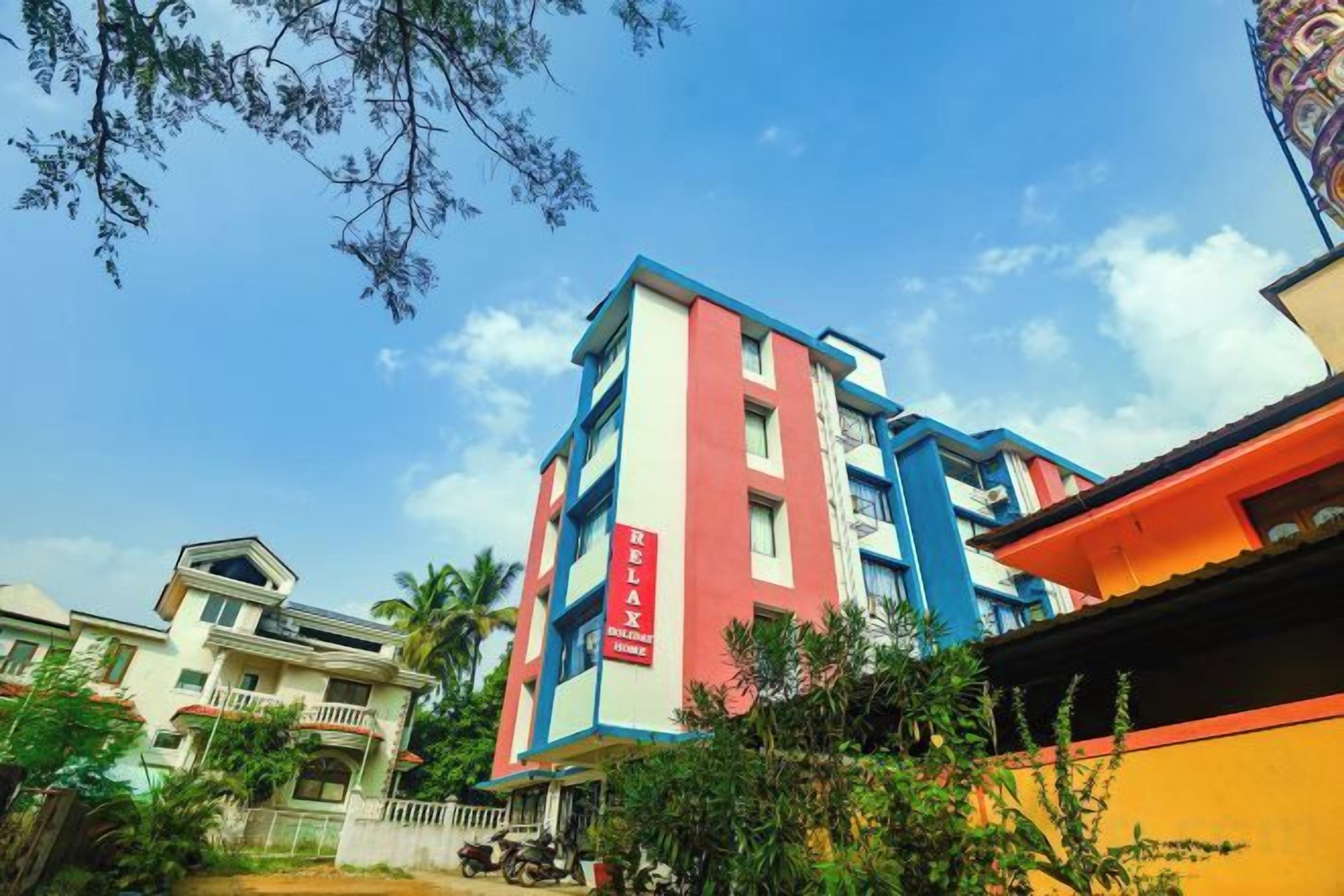 Un edificio de varios pisos con una fachada llamativa en rojo y azul, rodeado de vegetación y otros edificios.