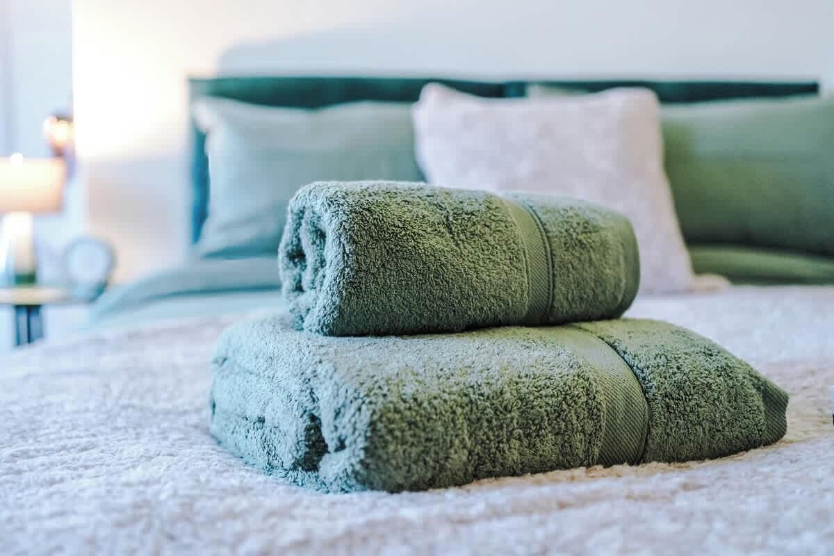 Un lit bien fait, avec des serviettes et des oreillers verts, une table de chevet avec une lampe et une tête de lit verte.