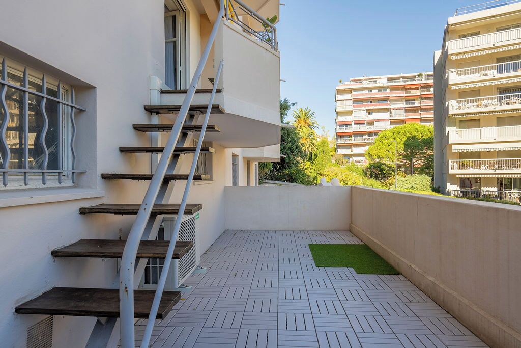 A residential building with a white exterior, a metal staircase, and a tiled balcony floor.