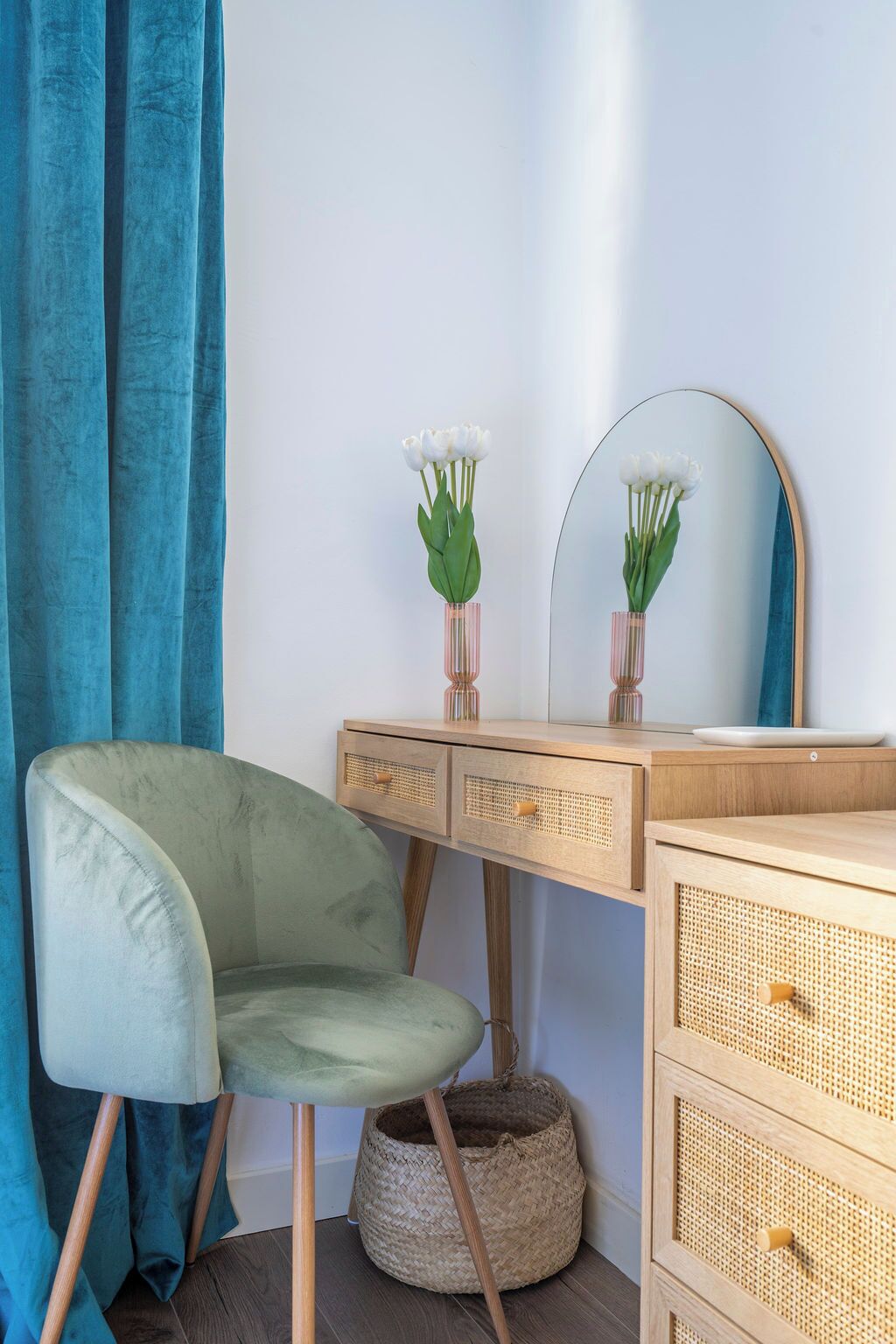 Ein Zimmer mit einem grünen Samtstuhl, einem hölzernen Schminktisch mit Spiegel und einem Korbwäscher.