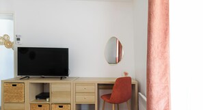 A room with a TV on a wooden desk, a red chair, a mirror, and storage baskets.
