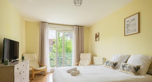 Une chambre d’hôtel avec un lit, une télévision, une chaise, un balcon avec vue et un tableau au mur.