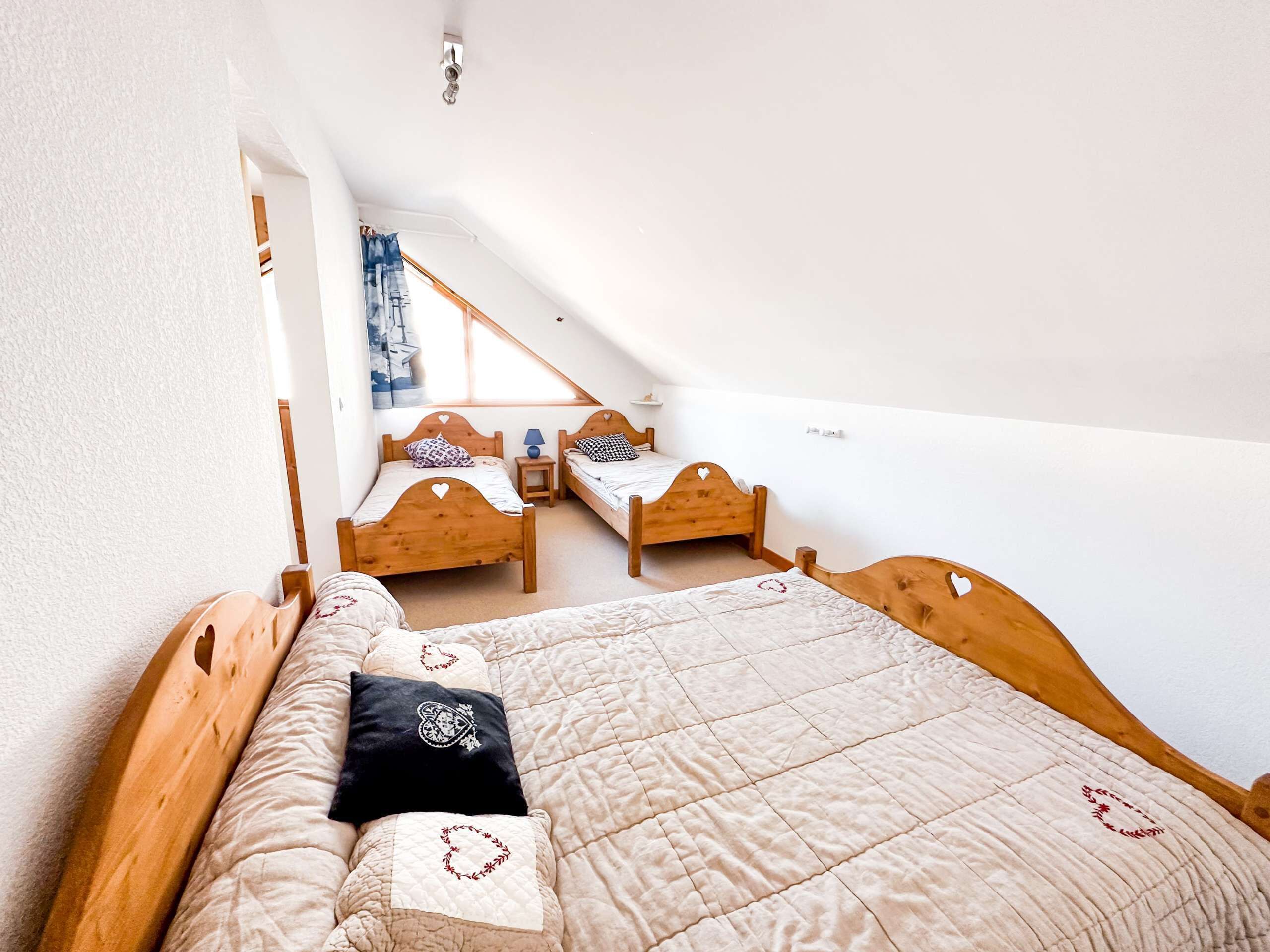 Un dormitorio con dos camas de madera, una ventana con cortinas y una mesita de noche pequeña.