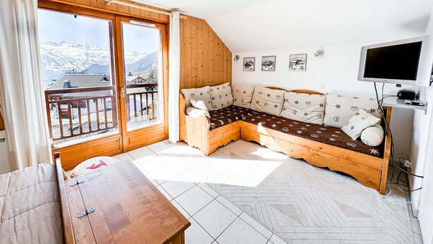 Et hyggeligt værelse med en træbænk, et fjernsyn og en balkon med udsigt til et bjerglandskab.