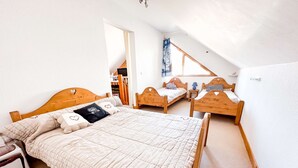 Et soveværelse med en stor seng, to mindre senge, et træhovedgærde og udsigt til en balkon.