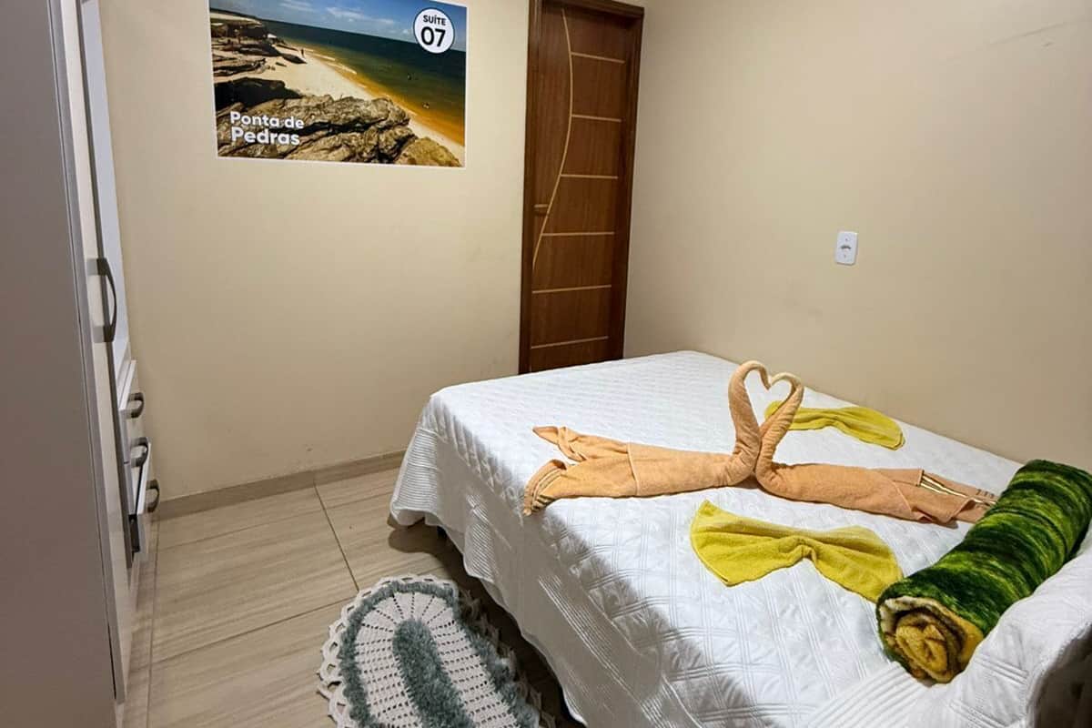 Een slaapkamer met een bed, een houten deur, een aan de muur hangend schilderij van een strand en een witte koelkast.