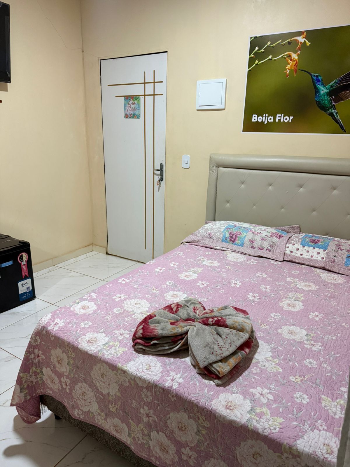 Ein Schlafzimmer mit floralem Bettbezug, einem gepolsterten Kopfteil und einer Tür mit einem Poster.