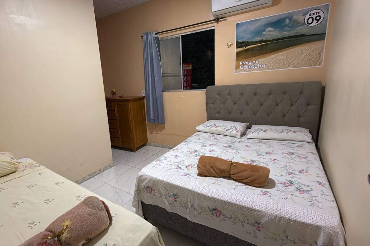 Een slaapkamer met een bed, een eenpersoonsbed, een raam met gordijn, een dressoir en een poster aan de muur.