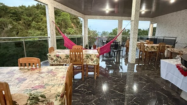 Ένας χώρος τραπεζαρίας με μαρμάρινο δάπεδο, ξύλινα τραπέζια και καρέκλες, με θέα στο πράσινο του εξωτερικού χώρου.