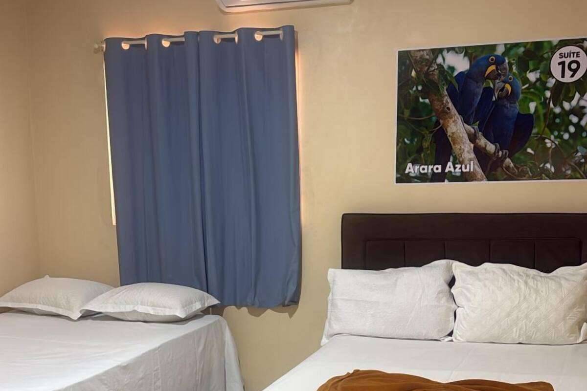 Een hotelkamer met twee bedden, een blauw gordijn, een airconditioner en een schilderij van papegaaien.