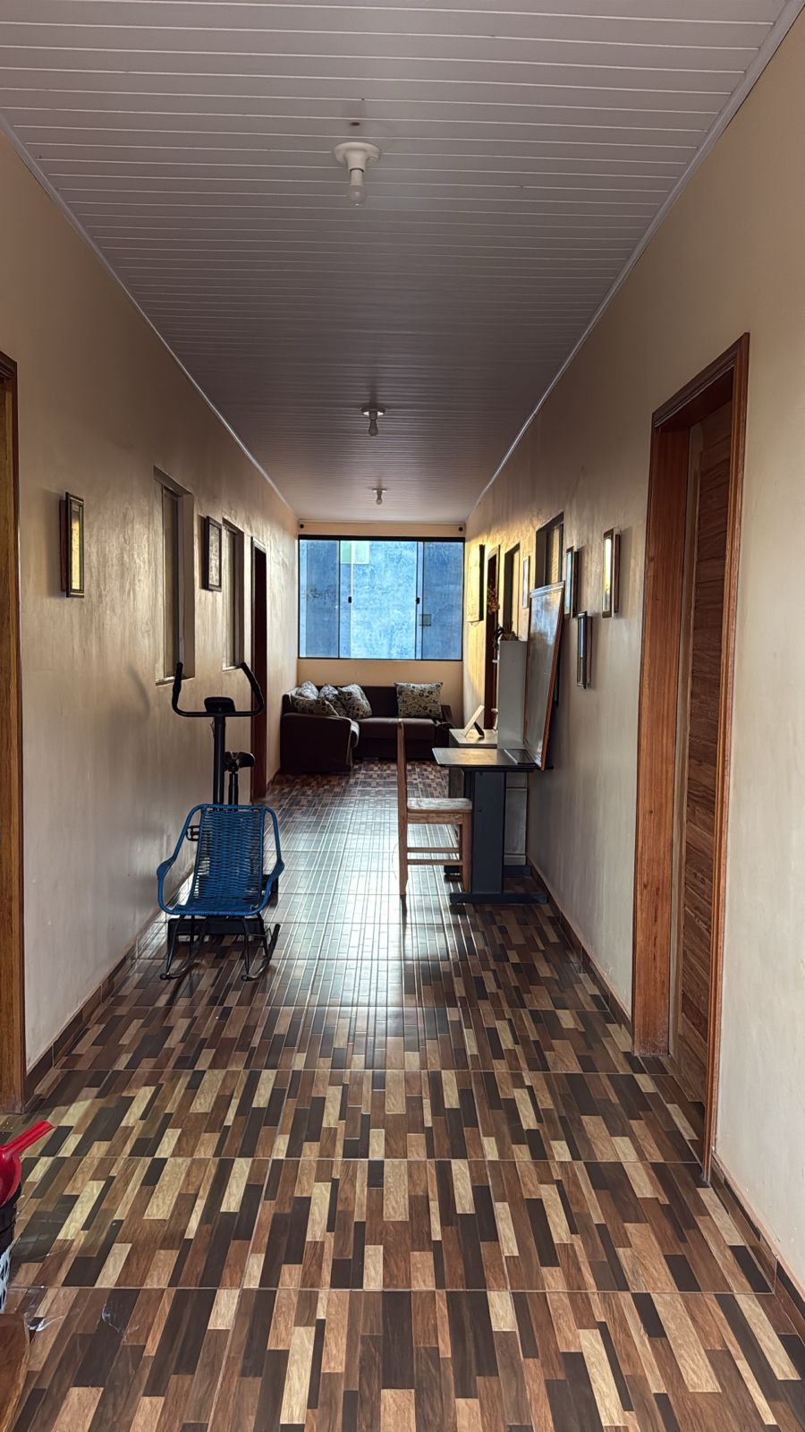 A hallway with a patterned floor, a row of framed pictures on the walls, and a window at the end.