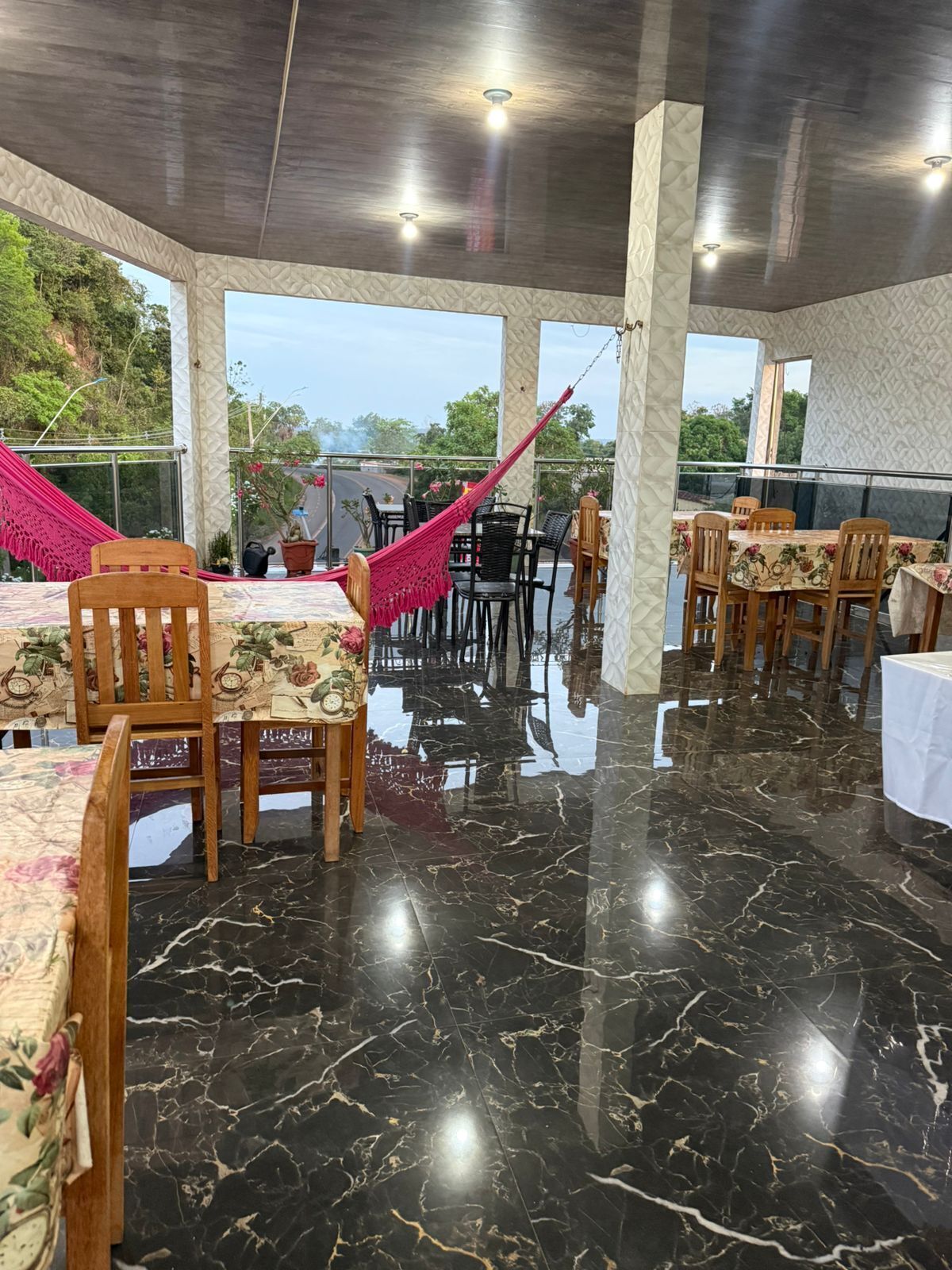 Un restaurant amb sòl de marbre, cadires de fusta i taules amb mantells florals.