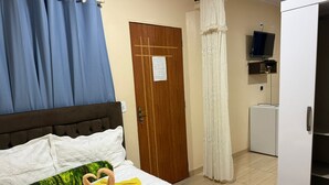 Ένα δωμάτιο ξενοδοχείου με ένα κρεβάτι, μια ξύλινη πόρτα, μια λευκή ντουλάπα και μια τηλεόραση τοποθετημένη σε ένα ράφι.