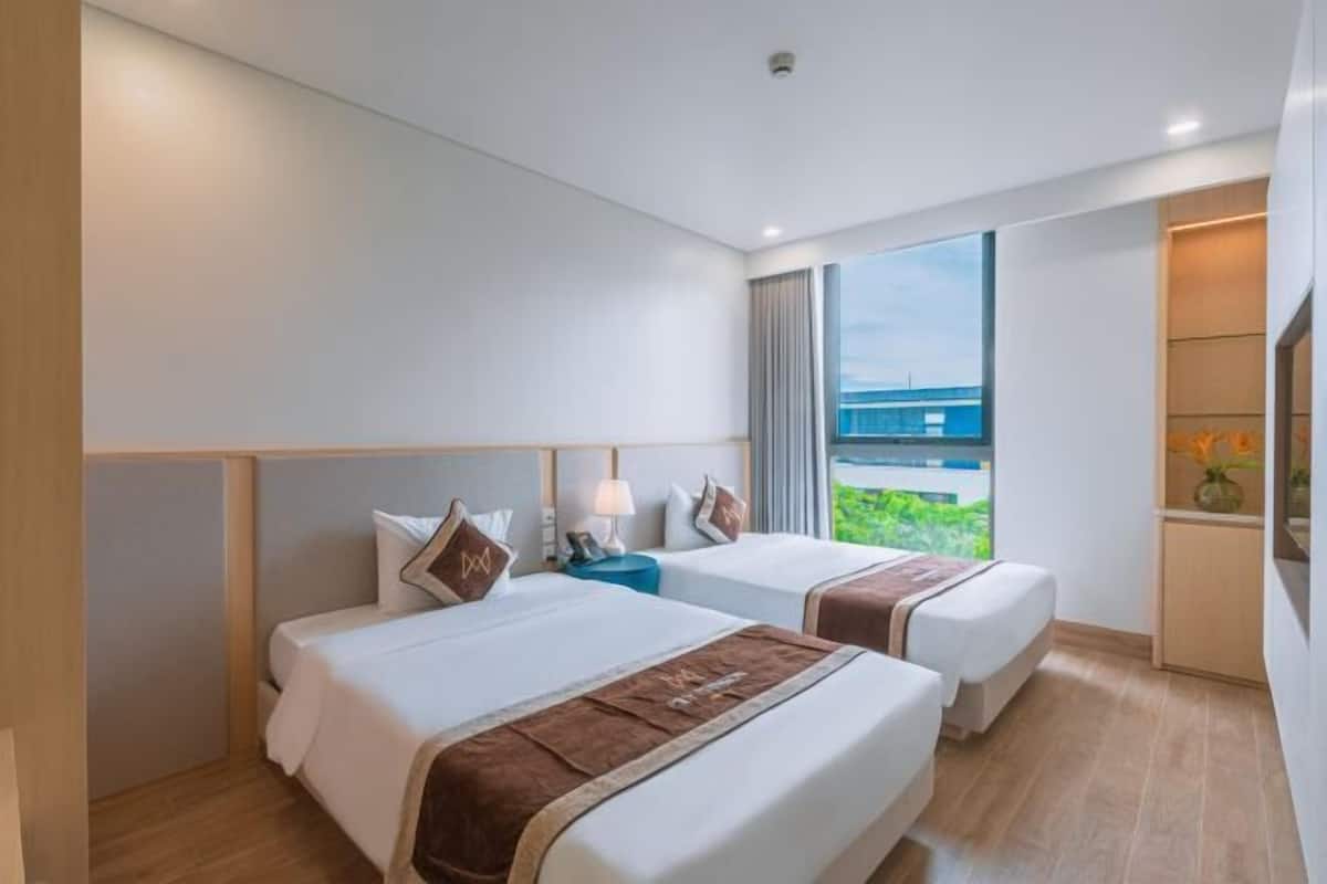 A hotel room with two beds, a nightstand, a lamp, a TV, and a window with a view.