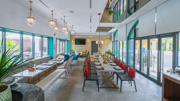 A modern restaurant with long communal tables, individual booths, and hanging pendant lights. - Mey Mansion Hotel Phu Quoc (Phu Quoc Island)