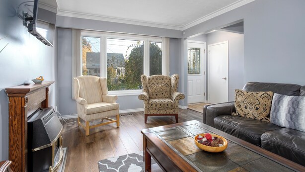 A living room with a fireplace, a sofa, a patterned armchair, and a large window with a view of trees. - Comfortable 3 bedroom unit on a quiet street,close to downtown (Guelph)