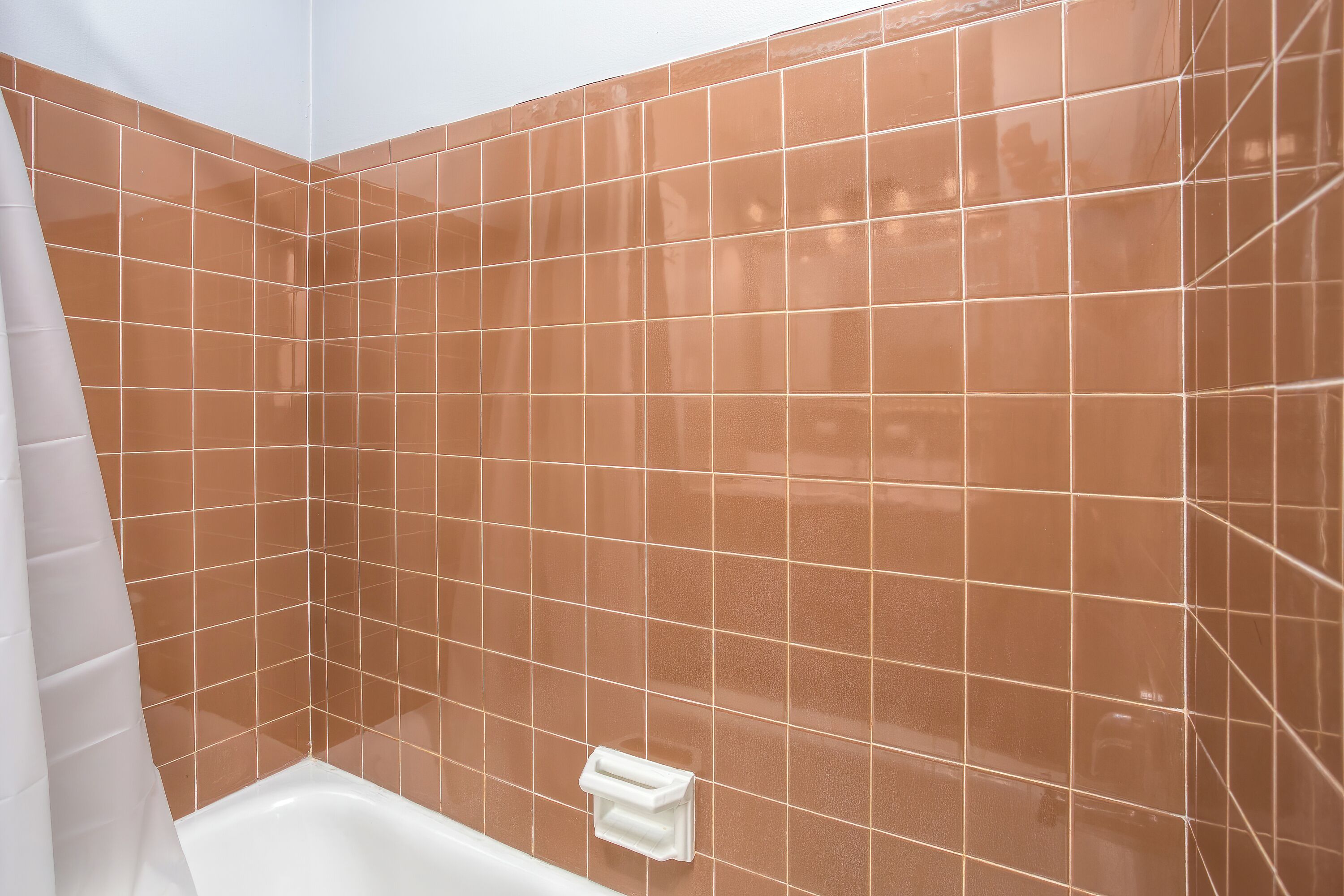 A bathroom with brown tiles, a white bathtub, and a white towel rack.