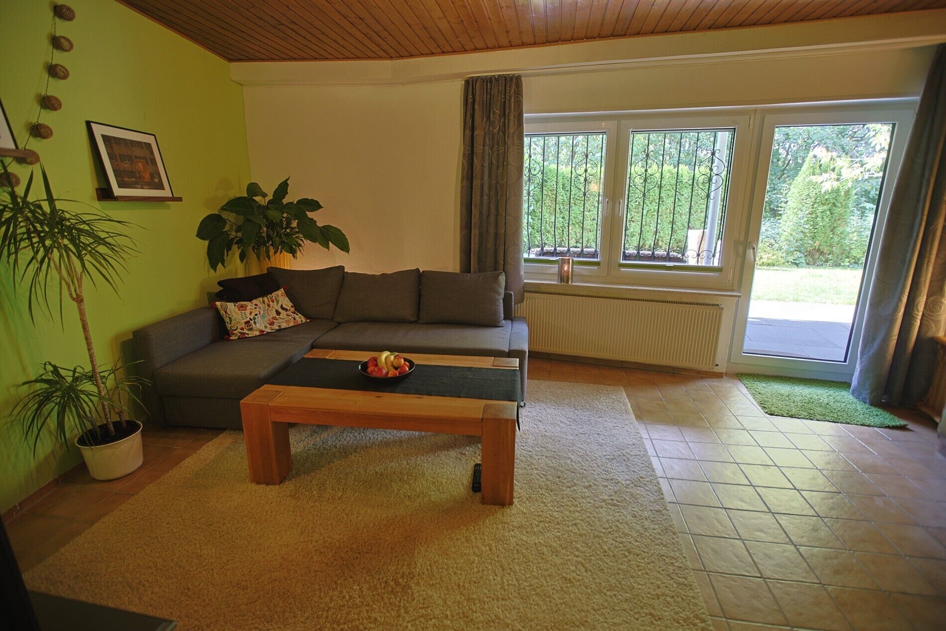 A living room with a sofa, coffee table, potted plants, and a window with a view of greenery.